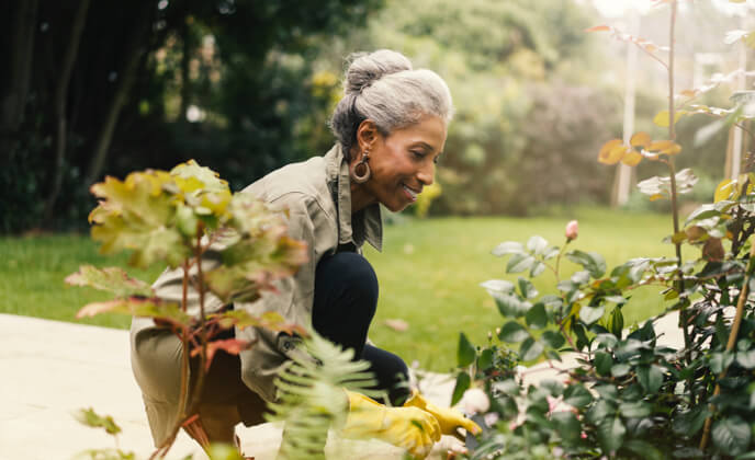 Seniorin kniet im Garten vor gruenen Pflanzen