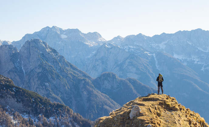 Bergsteiger steht auf Bergkuppe und schaut auf Bergkette