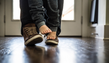 Baby-/Kinderfuesse stehen barfuss auf Schuhen von Vater